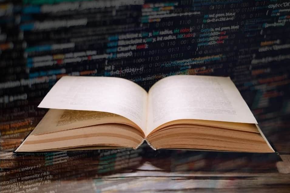 Im Vordergrund ist ein offenes Buch und im Hintergrund ein Code zu sehen