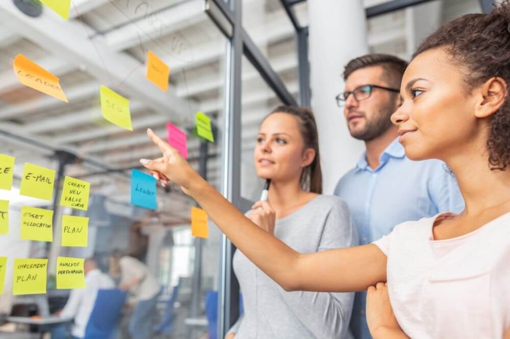 Several people standing at a glass board with sticky notes of different colors stuck on them
