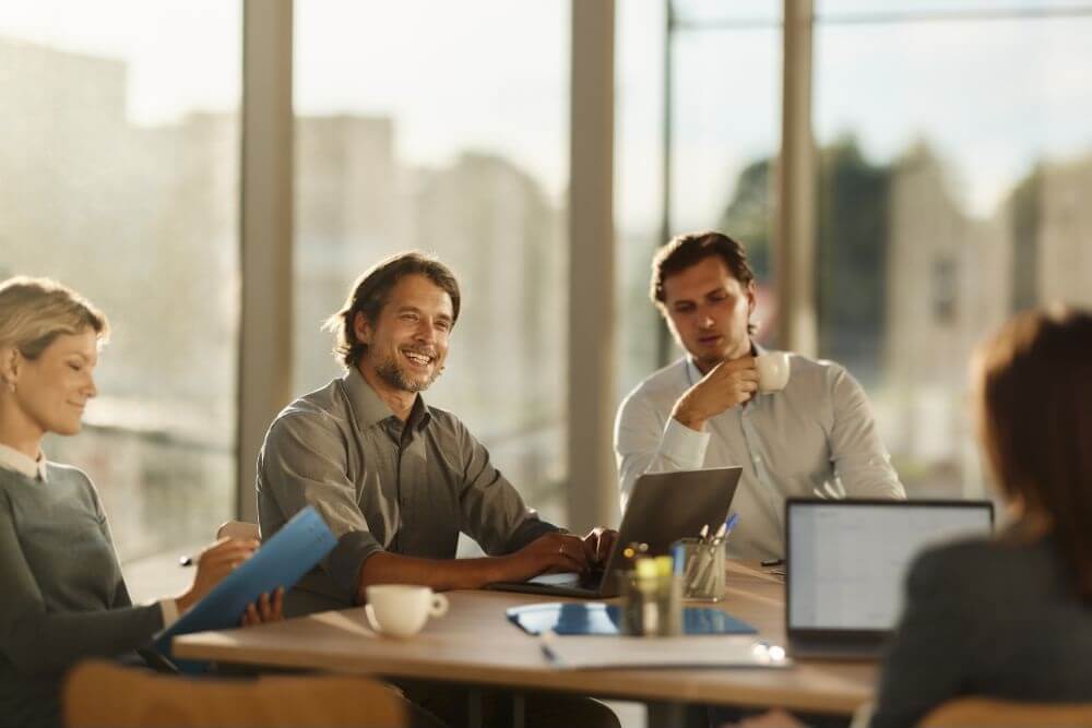 photo showing several people sitting around a table with computers and cups 