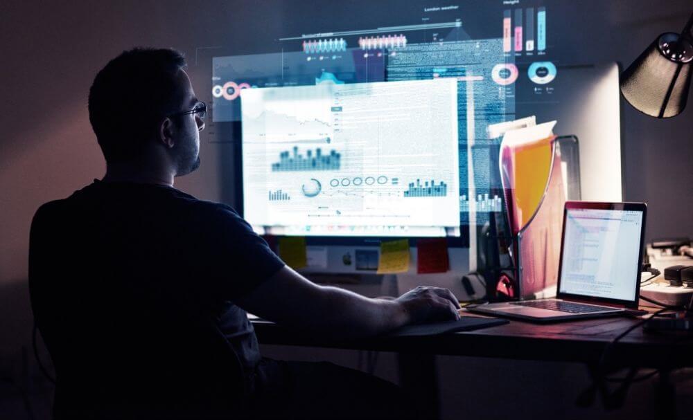 programista siedzący przy dużym monitorze w ciemnym pomieszczeniu